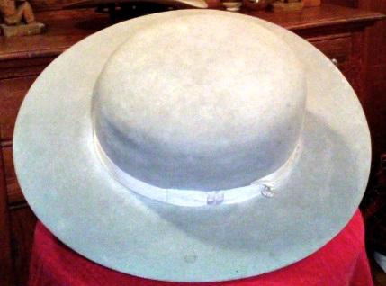 The Boss of the Plains, designed in 1865 by John B. Stetson, was a lightweight, all-weather hat created for the demands of the American West. It featured a high crown for insulation and a wide, stiff brim for protection from sun and precipitation, making it both durable and waterproof. Made from beaver felt, it took about 42 beaver belly pelts to produce a high-quality hat. The hat's design evolved over time, with various creases and brim shapes reflecting regional styles or individual preferences. The original design eventually inspired the modern cowboy hat. Popularized by entertainers like Buffalo Bill and Tom Mix, the hat became an essential part of the cowboy image. Later, Robert Baden-Powell adopted the Boss of the Plains-inspired campaign hat for the South African Constabulary and the Boy Scouts, further solidifying its place in popular culture.