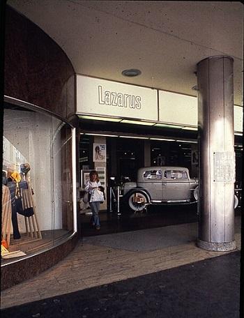 Photograph of a woman walking out of the South High Street entrance to the DowntownColumbus Lazarus Department Store, 141 South High Street. A classic automobile is on display just inside the entrance.